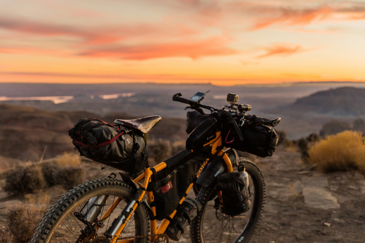 A mountain bike loaded with gear overlooking a desert vista against an orange sky